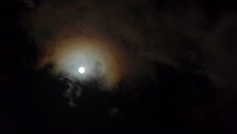 Bright-glowing-full-moon-with-clouds-passing-in-front,-looking-up-at-night-sky