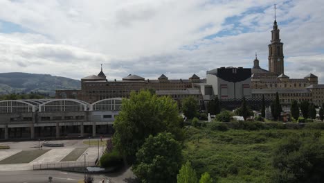 Rising-aerial-shot-of-La-Laboral-in-Gijon-with-clocktowers-and-mountains-in-the-distance