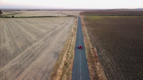 Aerial-tracking-red-car-on-country-road-tilts-up-to-flat-horizon
