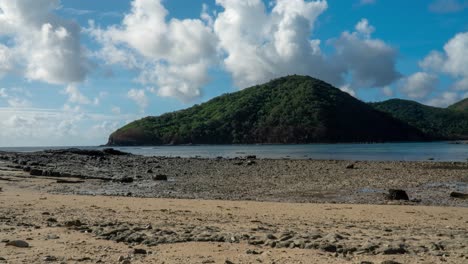 Falling-tide-on-tropical-island-small-bay-with-jungle-hill-in-Fiji,-clouds-rolling-by,-timelapse