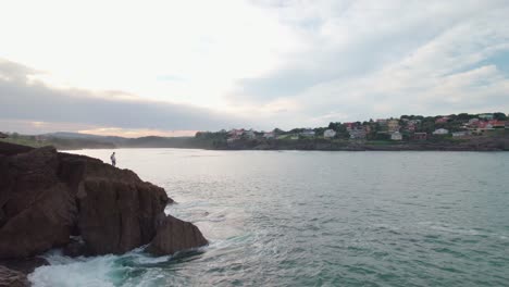 Silhouette-Eines-Fischers-Am-Ufer-Mit-Wellen-Und-Sonnenaufgang-Im-Hintergrund-In-Isla,-Einem-Dorf-In-Kantabrien,-Spanien