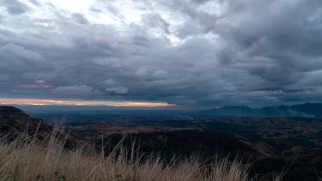 Sunset-on-Viti-Levu-island-with-dramatic-dark-clouds-in-sky,-grass-swaying-in-breeze,-timelapse