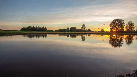 Timelapse-shot-of-sun-going-down-in-the-background-over-pristine-lake-along-rural-countryside-during-evening-time
