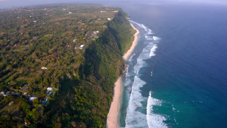 Birds-eye-view-of-the-majestic-cliffs-standing-tall-beside-coastline-of-beach-and-low-tides-moving-towards-them