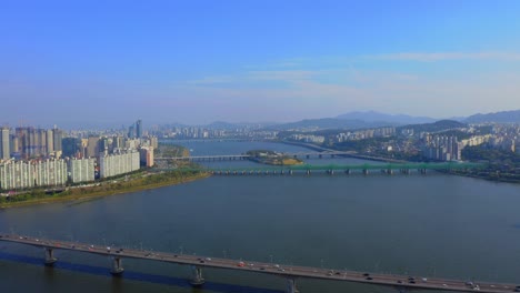 Drohnenschuss,-Der-Tagsüber-über-Dem-Han-Fluss-Mit-Sichtbarem-Wohngebiet-In-Der-Stadt-Seoul-Vorwärts-Fährt
