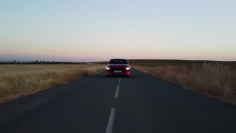 Low-POV-:-Shiny-red-vehicle-drives-on-country-road-at-dawn,-headlights