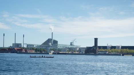 Kayak-sailing-by-industry-area-in-Copenhagen,-Denmark