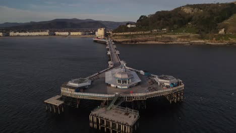 Aerial-drone-flight-around-the-pier-in-Llandudno-wales-showing-the-amusements-and-a-view-of-the-seafront-and-mountains