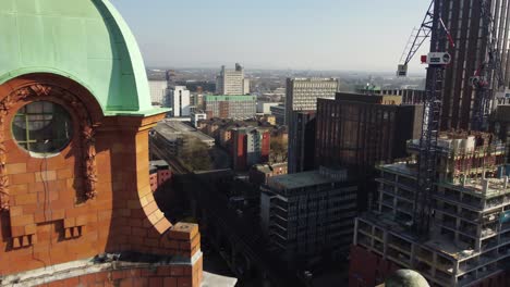 Arial-drone-flight-passing-by-the-green-dome-structure-of-the-clock-tower-on-the-Kimpton-Building-on-Oxford-Road-in-Manchester-City-Centre-with-a-view-of-new-developments-under-construction
