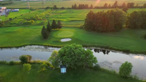 Luftdrohnenblick-über-Den-Golfplatz-Bei-Sonnenuntergang,-Teich-Und-Frische-Grüne-Vegetation