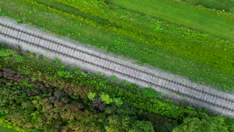 Train-Track-through-Green-Fields-Aerial-Drone-Top-Notch-Circles-Above-Rail-Road