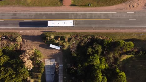 Aerial-drone-ascending-top-down-view-of-person-getting-off-white-bus-at-bus-stop-and-crossing-main-road-of-residential-area-of-El-Chorro-in-Uruguay