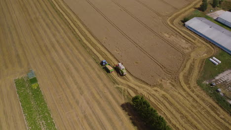Aerial-Overhead-View-Of-Harvester-And-Tractor-Beside-Each-Other-On-Golden-Wheat-Farmland
