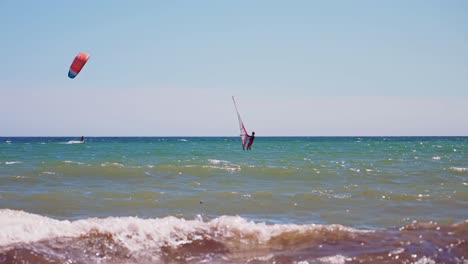 Windsurfen-Bei-Klarem-Himmel-Und-Einem-Vorbeiziehenden-Kitesurfer-Im-Hintergrund