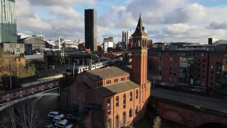 Aerial-drone-flight-over-Deansgate-Railway-Station-in-Manchester-City-Centre-showing-a-train-passing-by-over-a-bridge-and-pulling-into-the-station