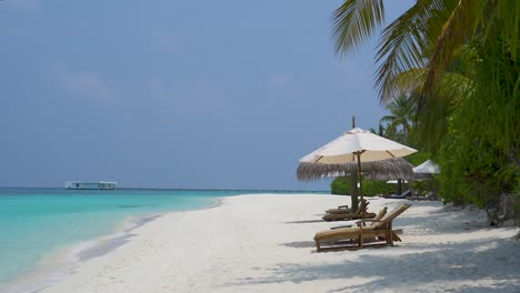Tropischer-Strand-Mit-Sanften-Wellen,-Palmen,-Liegestühlen-Und-Sonnenschirmen