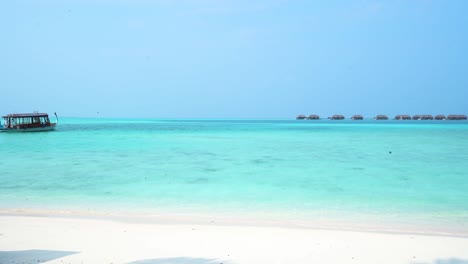 Barco-De-Maldivas-Moviéndose-A-Través-Del-Agua-Azul-Tropical-Hacia-Los-Bungalows-Sobre-El-Agua