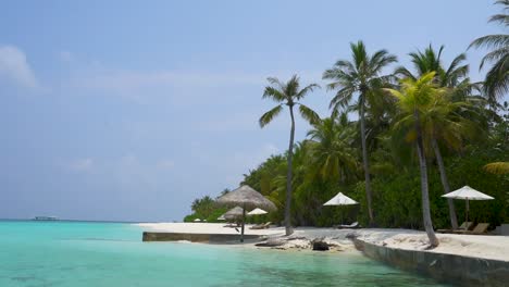 Playa-Tropical-Aislada-De-Maldivas-Con-Palmeras,-Arena-De-Aguas-Tranquilas-Y-Sombrillas