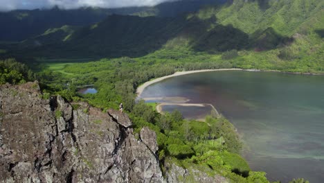 Hikers-on-Dramatic-Crouching-Lion-Cliff-overlooking-Hawaii's-Kahana-Bay,-Aerial-Orbit