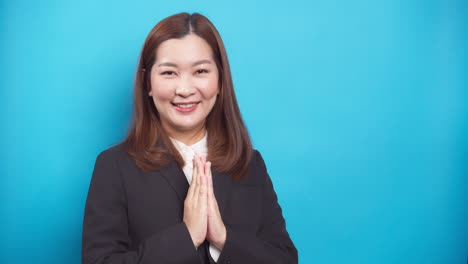 Schöne-Thailändische-Geschäftsfrau-In-Einem-Schwarzen-Anzug-Gäste-Sawadee-Mit-Einem-Lächeln-Auf-Blauem-Hintergrund