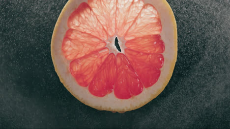 Grapefruit-Slice-Splashed-by-Strong-Water-Droplet-Mist-in-Slow-Motion-with-Backlit-Black-Background