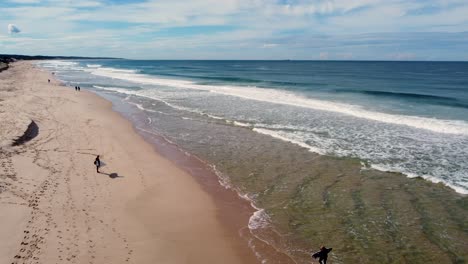 Drone-aerial-shot-of-surfer-and-people-waiting-on-sandy-beach-break-surfboard-Pacific-Ocean-waves-crystal-clear-travel-tourism-The-Entrance-Central-Coast-NSW-Australia-4K
