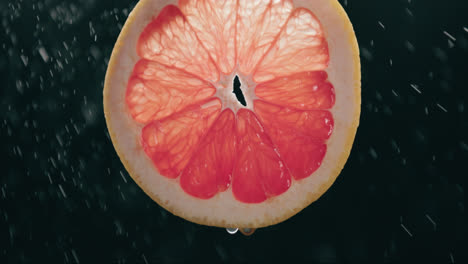 Fresh-Grapefruit-Slice-Splashed-by-Water-Droplet-Mist-in-Slow-Motion-with-Backlit-Black-Background