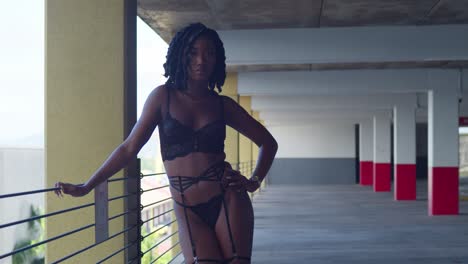 Sexy-African-woman-wearing-lingerie-and-high-heels-leans-over-the-railing-in-a-parking-garage-on-a-sunny-day