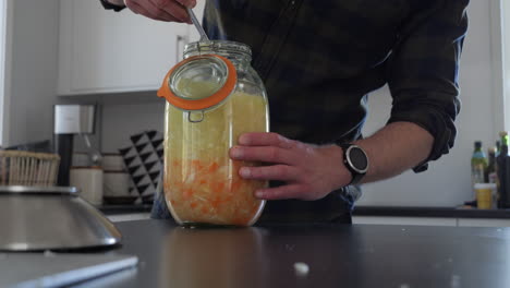 Medium-shot-of-person-fermenting-food-in-glass-jar-at-home-kitchen