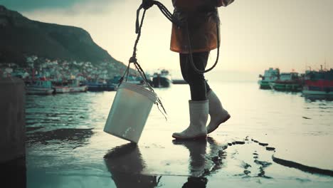 Fisherman-is-filling-a-bucket-full-of-seawater-and-pulling-it-out-on-the-platform-deck,-slow-motion