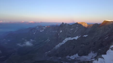 Wide-aerial-view-from-drone-over-Alps-with-snow-on-steep-rocky-slopes-at-sunrise