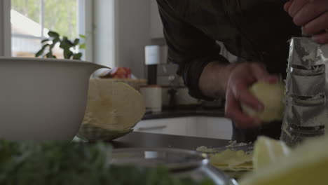 Man-shredding-vegetable-to-ferment-at-kitchen-counter-at-home,-slider-movement