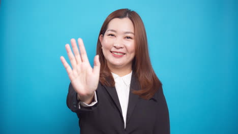 Porträt-Der-Asiatischen-Glücklichen-Geschäftsfrau-Winkt-Mit-Der-Hand-Für-Werbung,-Die-Auf-Blauem-Hintergrund-Isoliert-Ist