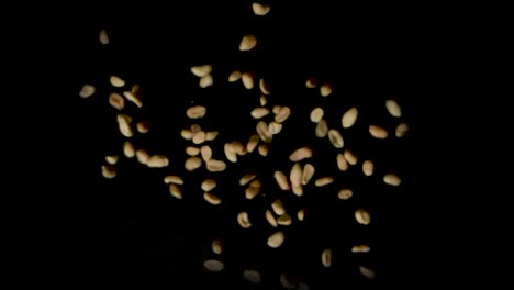 Static-shot-of-a-pile-of-shelled-peanuts-suddenly-exploding-outward-then-transiting-into-slow-motion-then-falling-to-the-ground-on-a-black-background