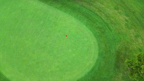 Drone-shot-over-perfectly-manicured-putting-green,-flagstick-with-red-flag