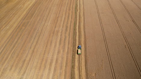 Aerial-top-down-shot-of-tractor-transporting-fresh-cutted-wheat-grain-on-field-during-sunny-day