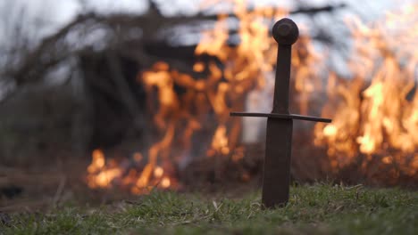 Metal-sword-in-front-of-a-burning-fire,-middle-age-concept,-strong-fire-in-background