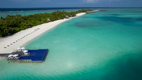 Luftaufnahme-Des-Inselstrandes-Der-Malediven-Mit-Überwasser-Pool-Liegestühlen,-Palmen-Bungalows-Durch-Seichtes,-Klares,-Blaues-Wasser