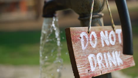 "Do-Not-Drink"-sign-hangs-on-the-back-of-an-old-iron-faucet-pouring-water-out-on-a-summer-day