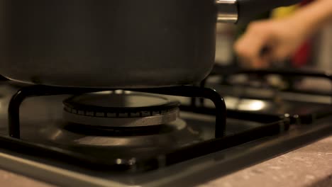 Placing-pot-on-stove-and-turning-gas-stove-on-close-up,-slow-motion