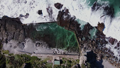 Waves-crashing-next-to-iconic-marine-tide-pool-in-Hermanus,-drone-time-lapse