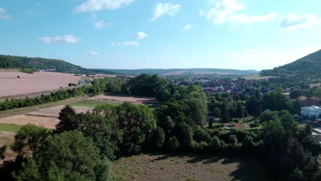 Fly-over-trees-with-a-view-of-the-start-of-sondershausen-village-during-a-summer-day