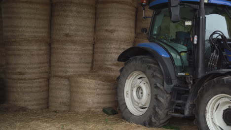 Medium-shot-of-a-blue-tractor-parked-infront-of-hay-balls