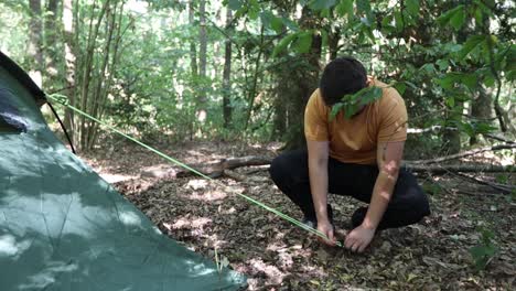 Disappointed-man-pitches-a-tent-at-a-campsite-in-the-woods-but-fails-to-put-the-hook-in-the-ground-twice-and-drops-the-string
