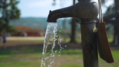 Water-comes-pouring-out-of-an-old,-vintage-faucet-in-an-outdoor-park-on-a-summer-day