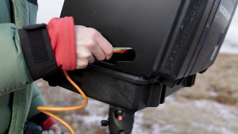 Outdoor-photographer-plugging-in-orange-USB-c-cable-into-laptop-on-stand