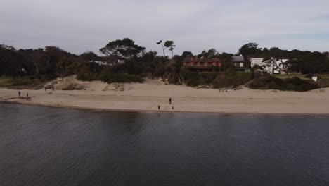 Aerial-tracking-shot-of-two-kids-playing-on-sandy-beach-at-Maldonado-River-in-Uruguay