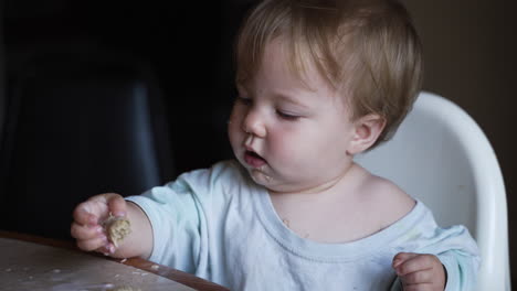 Cute-baby-girl-with-blue-eyes-eating-breakfast-in-highchair