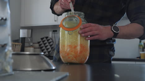 Man-Pressing-Fermented-Vegetables-or-Sauerkraut-in-Jar,-Close-Up