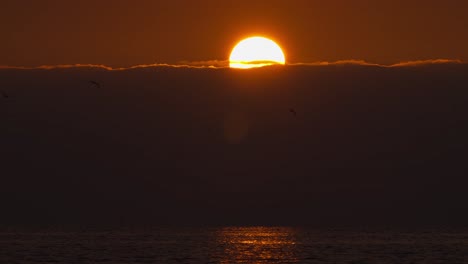 Sunrise-over-cloudy-sky-horizon-time-lapse-of-ball-of-red-yellow-warm-sun-over-ocean-sea-coastline